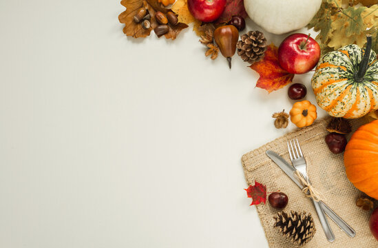 Autumn flat lay composition with copy space on white background. Pumpkins, apples, cones, leaves, acorns, chestnuts, with fork and knife on a jute material for Thanksgiving dinner.