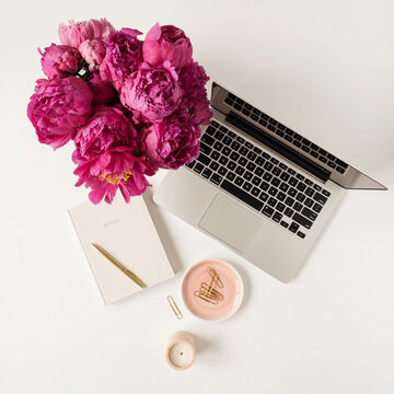 Laptop, beautiful pink peony tulip flowers bouquet and notebook on white table background. Flat lay, top view minimalist home office desk workspace.