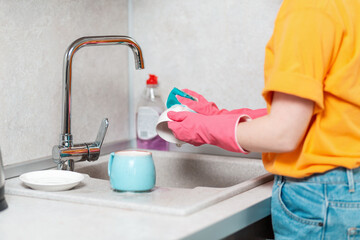 A housewife in casual clothes and pink rubber gloves is washing a cup. Close up of hands