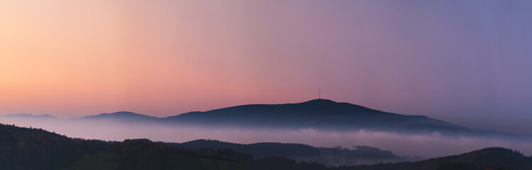 misty landscape at sunset, mountains rising from clouds of fog in the background, clear sky - mountain Klet, Czech republic