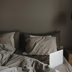 Modern interior design concept. Hygge styled bedroom with grey washed linen bedclothes, pillows, laptop. Minimalistic nordic living room.