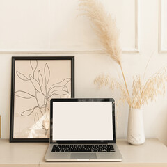 Laptop computer with blank screen pastel beige on table with boho decorations. Pampas grass bouquet, home plant. Minimal boho styled interior design template with mockup copy space.