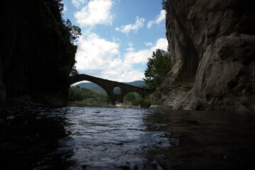 The beginning of a magnificent Gorge, with the silhouette of a stone bridge to appear at background and visitors near it. During the summer period, Portitsa, Grevena, Greece.