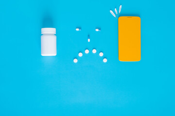safe self-isolation. sad smiley face with pills, phone on a blue background.