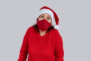 Fototapeta na wymiar Mature surprised woman in a red protective mask, in a santa hat on a gray background. Christmas, New Year in quarantine