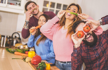 Group of friends cooking togheter organic food at home while having fun with bio vegetables