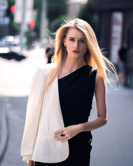 Fashionable girl walks down the street in a black dress and a white jacket