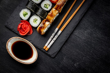 Japanese rolls on black slate board and black background top view, close-up, free space for text