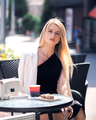 Girl posing at a table in a cafe in the city in a sexy black dress