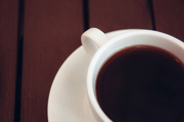 Black coffee with foam in a white ceramic cup on a wooden table. Selective focus. Breakfast in a cafe