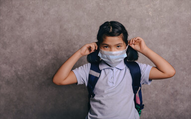 Elementary school girl with face mask going back to school after covid-19 quarantine and lockdown. Kid in masks for coronavirus prevention.