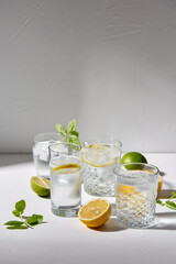 drink, detox and diet concept - glasses with fruit water or lemonade, lemons, limes and peppermint on white table