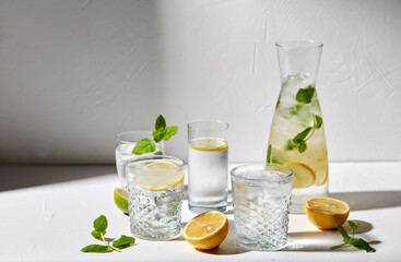 drink, detox and diet concept - glasses with fruit water or lemonade, lemons, limes and peppermint on white table