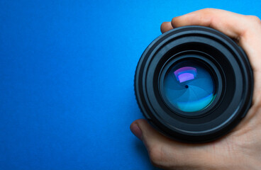 Holding camera lens in hand with blue reflection and colorful neon glares against light blue...