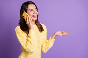 Photo portrait of happy woman talking over yellow smartphone holding blank space in hand isolated on vivid purple colored background