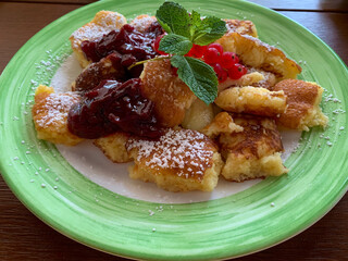 Traditional austrian bavarian sweet dish kaiserschmarrn with powdered sugar and plum sauce on the green decorative plate high angle view