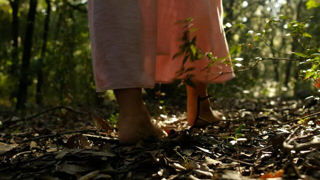 barefeet woman walking in the woods with long dress. young person walking in the wilderness. contact and unity with pristine nature and natural light. pink dress