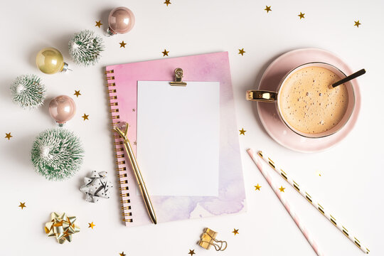 Desktop blank planner. Flat lay of white working table background with cup of coffee and Christmas decoration. Top view balls, fir tree, paper clips, mock up greeting card, craft Notebook and pen.