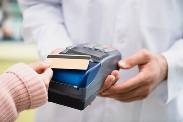 partial view of pharmacist holding payment terminal while customer paying by credit card in drugstore