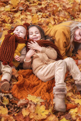 Magical Golden autumn, beautiful blonde mother with her daughter and son in red scarves playing and laughing in the maple forest, autumn holidays