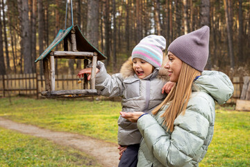 Family at autumn park. Young mother shows her daughter bird feeder outside.