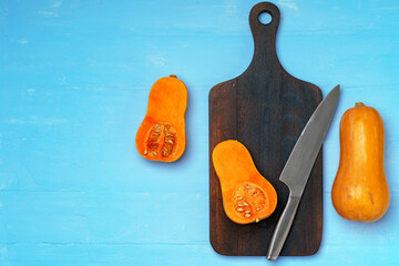Small pumpkin cut into halves on wooden cutting board with knife