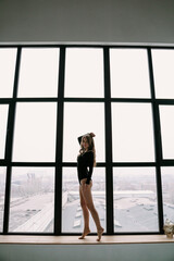 Fototapeta na wymiar Beautiful blonde girl in a black bodysuit near a large window