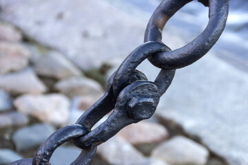 Old forged rusty chain with peeling paint on the background of paving stones.