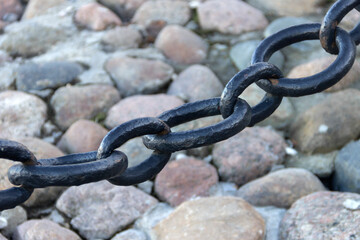 Old forged rusty chain with peeling paint on the background of paving stones.