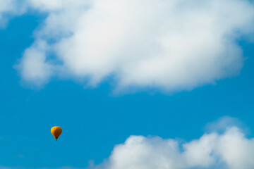Yellow hot air balloon in blue sky with white clouds