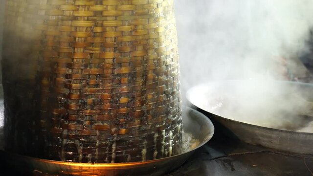 Coconut sugar production process. Coconut nectar or coconut sap was boiling and stir in the wok over the fire stove. Bamboo basket cover  wok letting boiling water to flow out and refill to the wok.