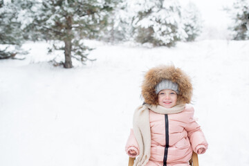 Little girl in a fur-trimmed hat laughs while sledding in winter
