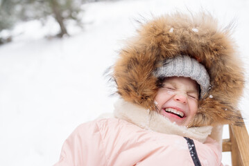 Little girl in a fur-trimmed hat laughs while sledding in winter
