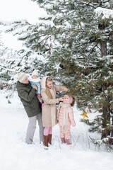 Young dad and mom and their little daughters on a family walk in the forest decorate the christmas tree for christmas
