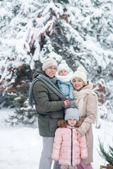 Fototapeta na wymiar Young family - mom, dad and two children go for a walk in the winter snowy forest 
