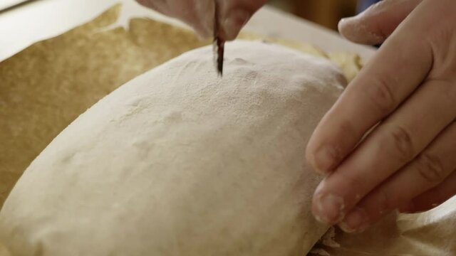 Close up hands cutting a pattern on the sourdough bread loaf
