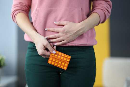 Woman with pills in hands holding lower abdomen at home closeup. Treatment of reproductive system of women concept