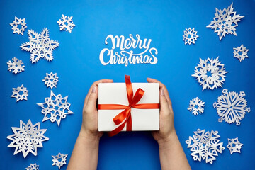 Merry Christmas greeting card with gift box and paper snowflakes on blue