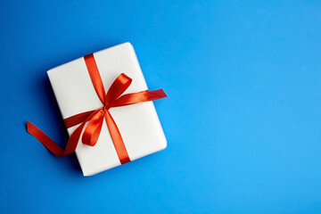 White gift box tied with red ribbon on blue background