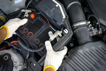 The auto mechanic is replacing the car battery in engine compartment.	