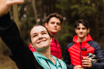 Obraz premium Young woman taking a self-portrait with her friends - Group of friends posing for a selfie in the forest.