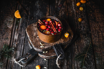 mulled wine with cinnamon, spices, berries and fruits in metal pot, brown wooden background, winter warming beverage, copy space