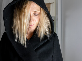 BLOND SPANISH WOMAN DRESSED IN BLACK, WITH HOOD IN THE ROOM OF HER HOUSE, SHOWING SADNESS, ANGER, BITNESS, PESIMISM