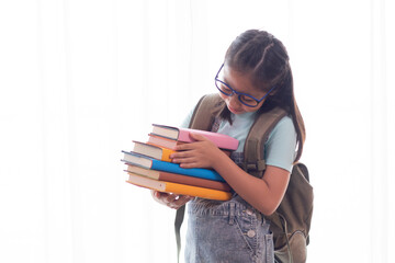 Adorable Asian smart girl in casual jean hold stack of books, adorable intelligent school girl primary looking her many book with happy, girl study at home social distance back to school concept