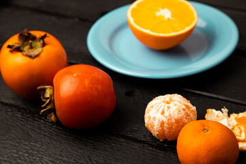Orange persimmon and tangerine on black background