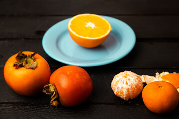 Orange persimmon and tangerine on black background