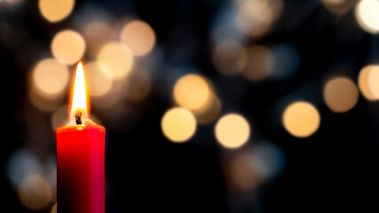 a red candle burns in the foreground in front of a colorful bokeh background