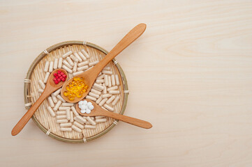 Healthy lifestyle - Vitamins, minerals and nutritional supplements in wooden spoons inside a braided bamboo plate. Isolated on wooden background. Top view. Copy space.