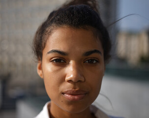 Here and Now. Close up portrait of pretty young mixed race woman looking focused at camera while posing outdoors on a sunny day. Selective focus. Medium format shot