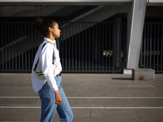 Walking the streets. Young mixed race woman in casual wear walking around the city on a warm sunny day. Selective focus. Medium format shot. Side view